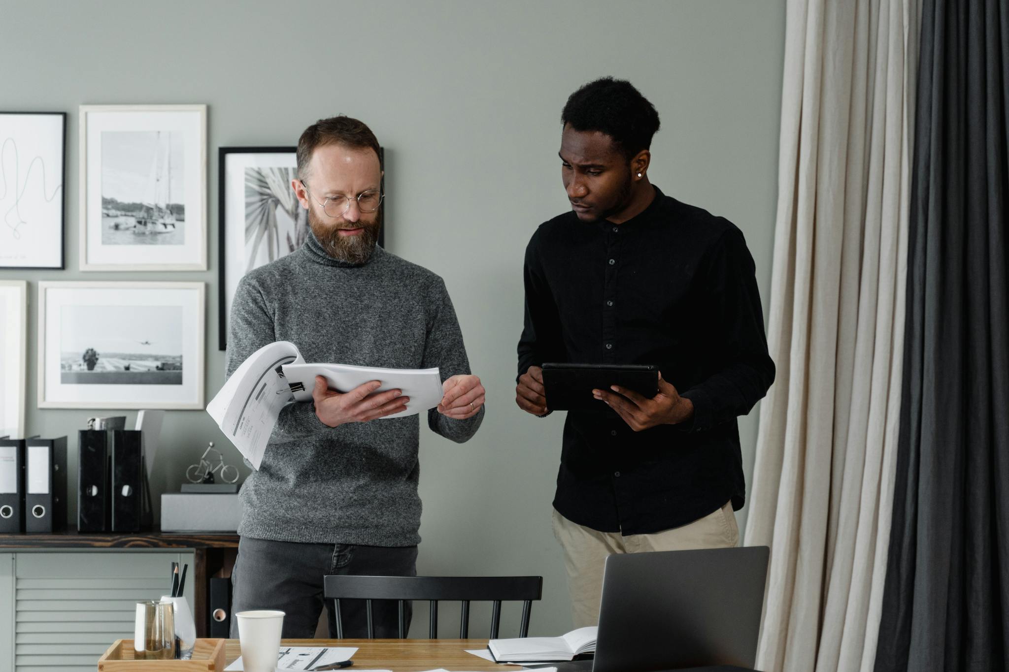 Two professionals reviewing documents and using a tablet in a modern office setting.